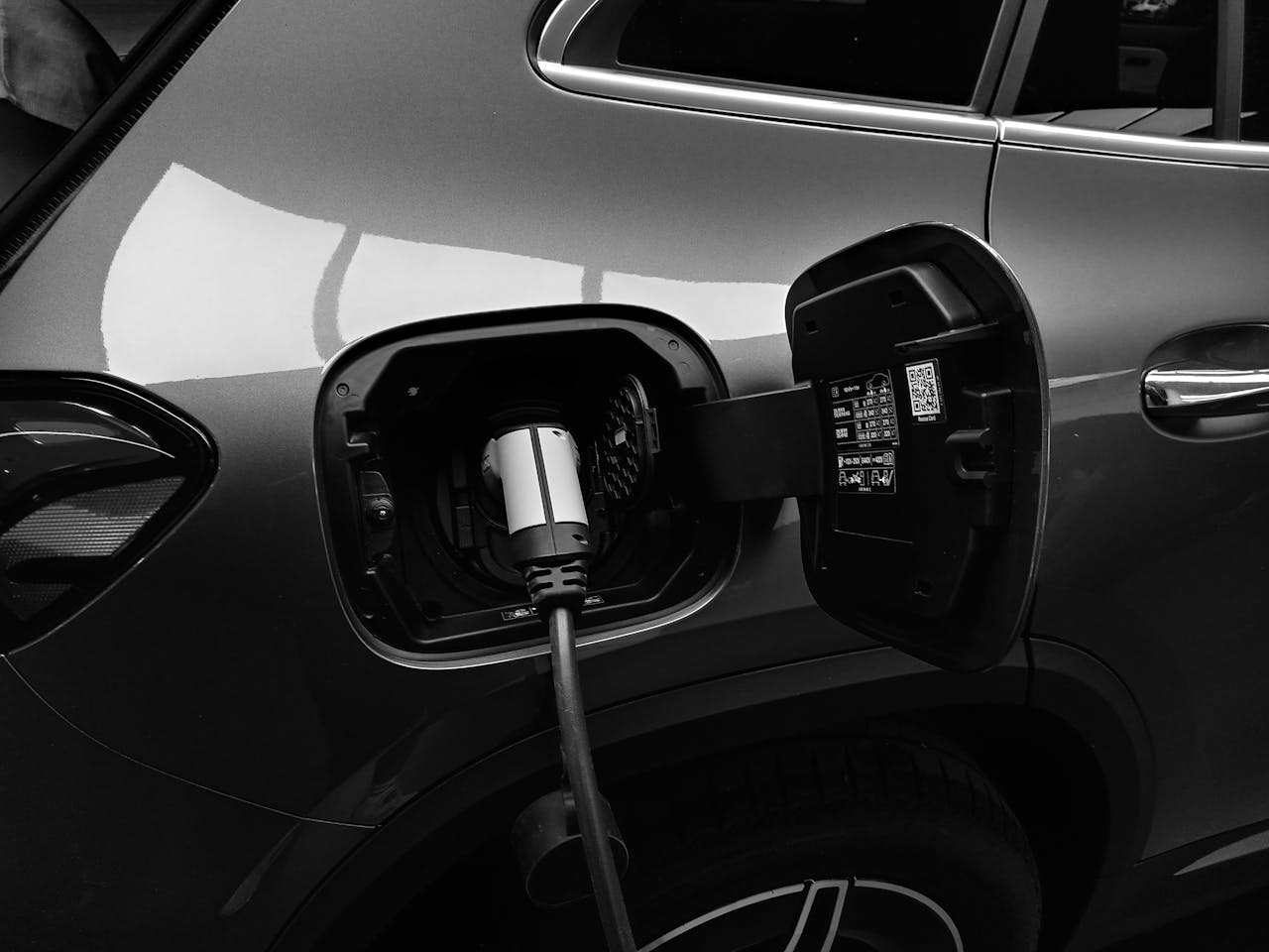 Home Close-up black and white image of an electric vehicle charging at a station.